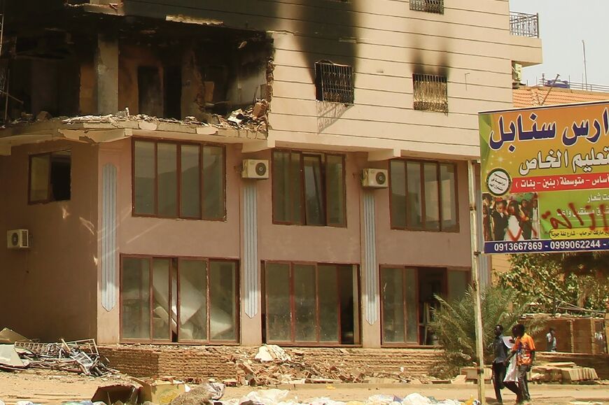 Men walk past a building damaged during battles between the forces of two rival Sudanese generals in the southern part of Khartoum, on April 23, 2023