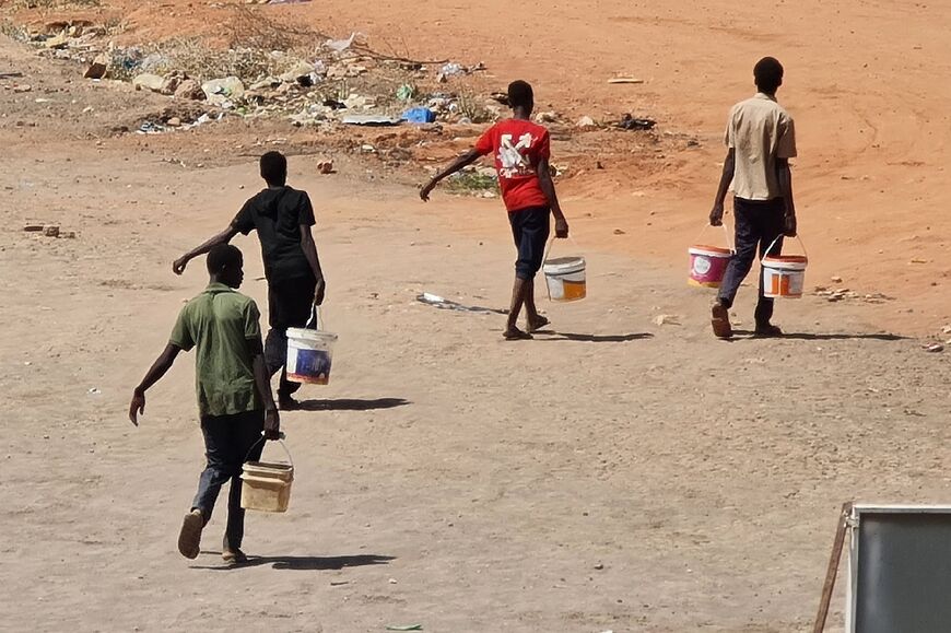 Youths carry buckets of water in Khartoum, where the fighting has cut of water supplies