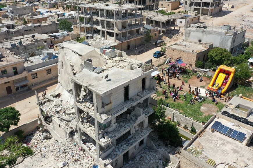 Quake-damaged buildings in Jindayris in Syria's rebel-held Aleppo province, seen on April 21, 2023 next to a children's  amusement park set up at the end of the Muslim holy fasting month of Ramadan