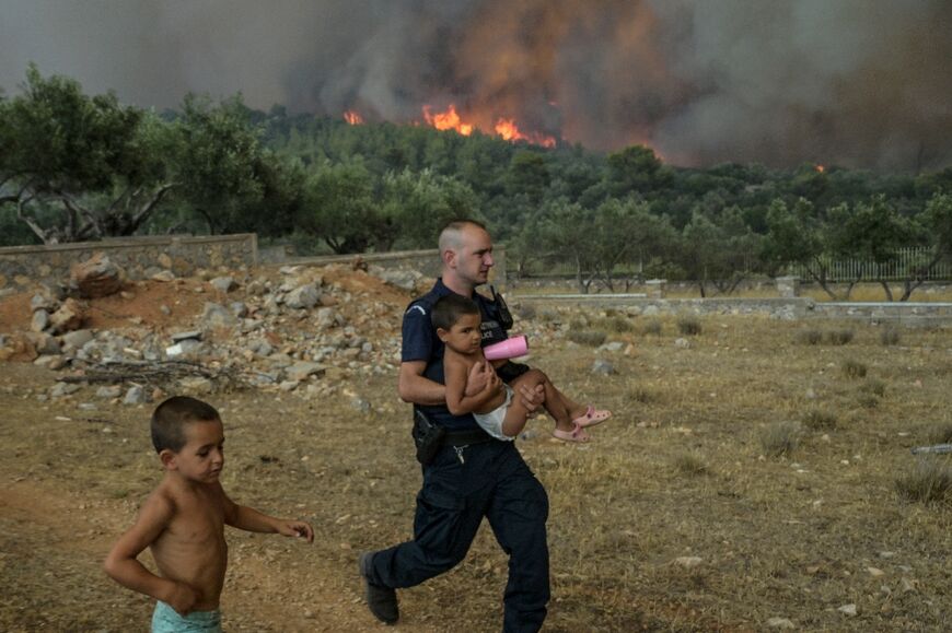 A Greek policeman evacuates a child from wildfire at the village of Agios Charamlabos, near Athens 