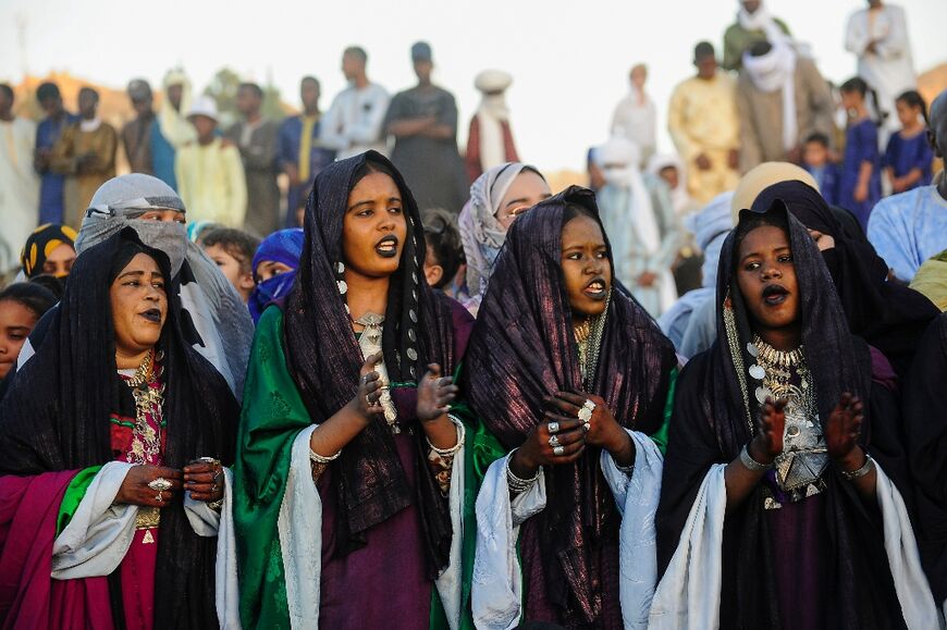 Women sing and beat the tambourine, adorned with glittering jewellery and henna tattoos