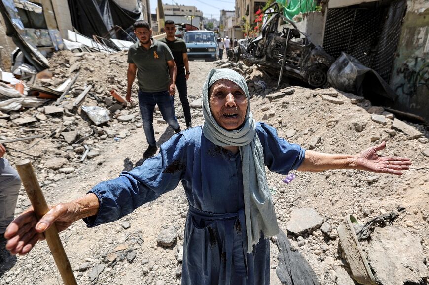 An elderly woman stands amid the rubble of broken pavement in an alley in Jenin 