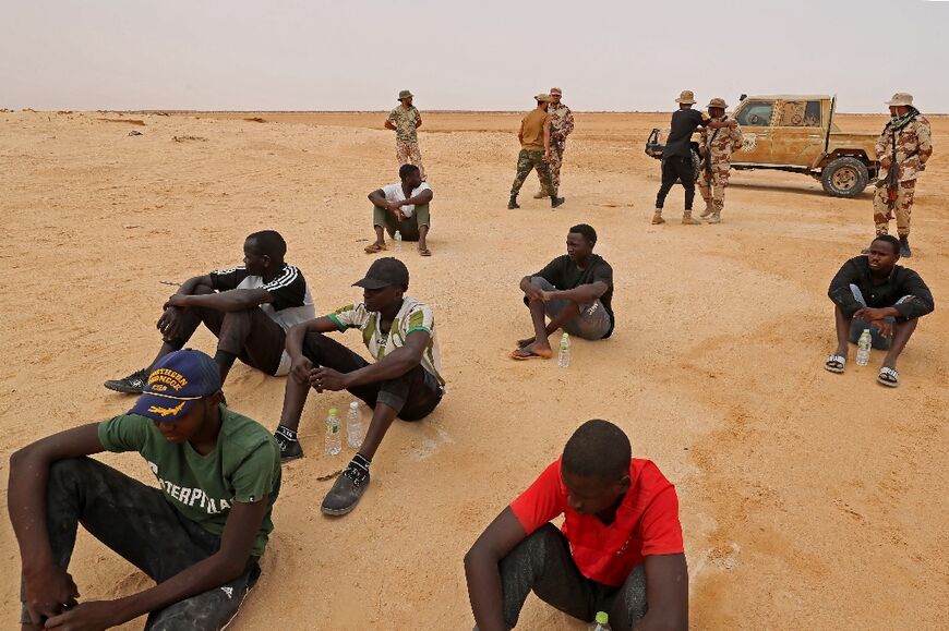 Libyan border guards stand behind black African migrants reportedly abandoned in the desert by Tunisian authorities