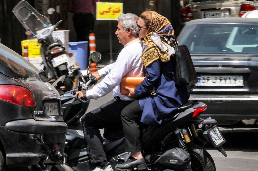 A woman rides behind a man on a scooter through traffic in central Tehran on September 4, 2023