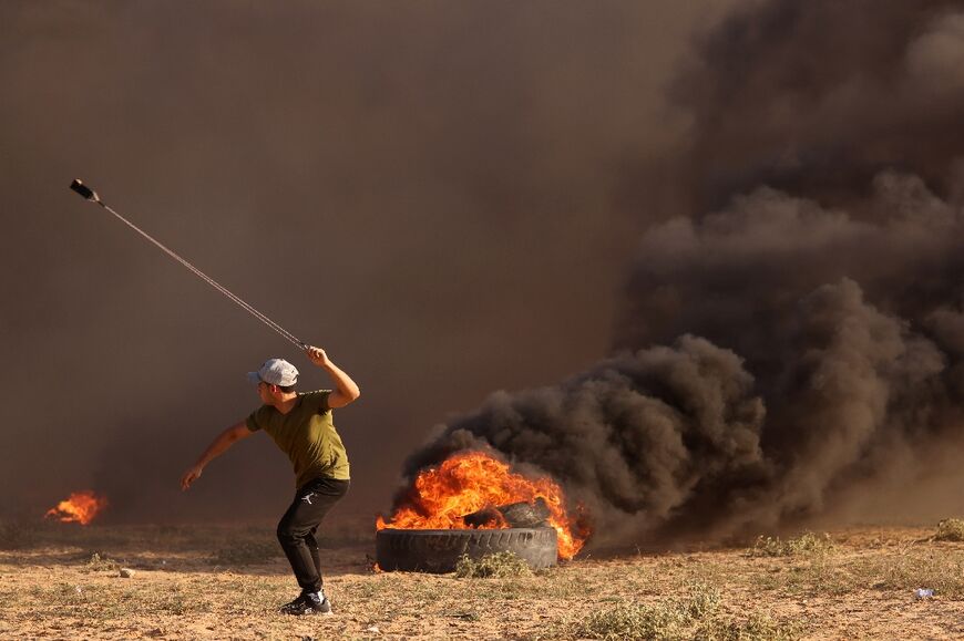 A Palestinian demonstrator hurls rocks towards Israeli soldiers guarding the Gaza border