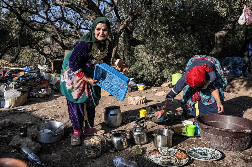 Village women prepare food outside using utensils recovered from the rubble of their homes and a shared wood fire