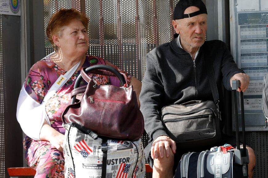 People with their luggage wait at a bus stop in the northern Israeli town of Kiryat Shmona on the border with Lebanon, to be evacuated to a safer location on October 22, 2023