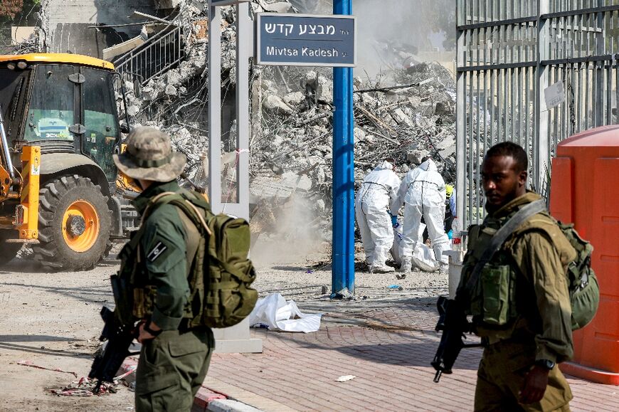 Israeli soldiers patrol as volunteers remove the bodies of killed Palestinian Hamas militants from outside the police station in Sderot on October 11, 2023 