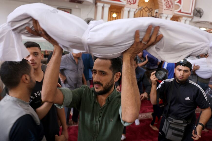 During a group funeral, a man carries the draped body of a child from the Palestinian Abu Hilal family, who was killed with other relatives in an Israeli airstrike that hit their home in Rafah, Gaza