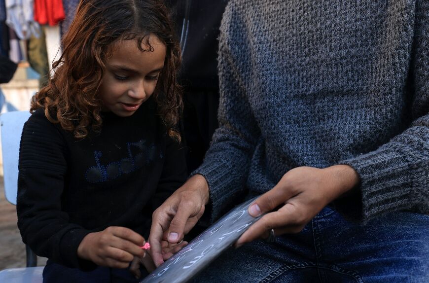 A displaced Palestinian child writes on a board as she follows an English lesson taught by Ennabi
