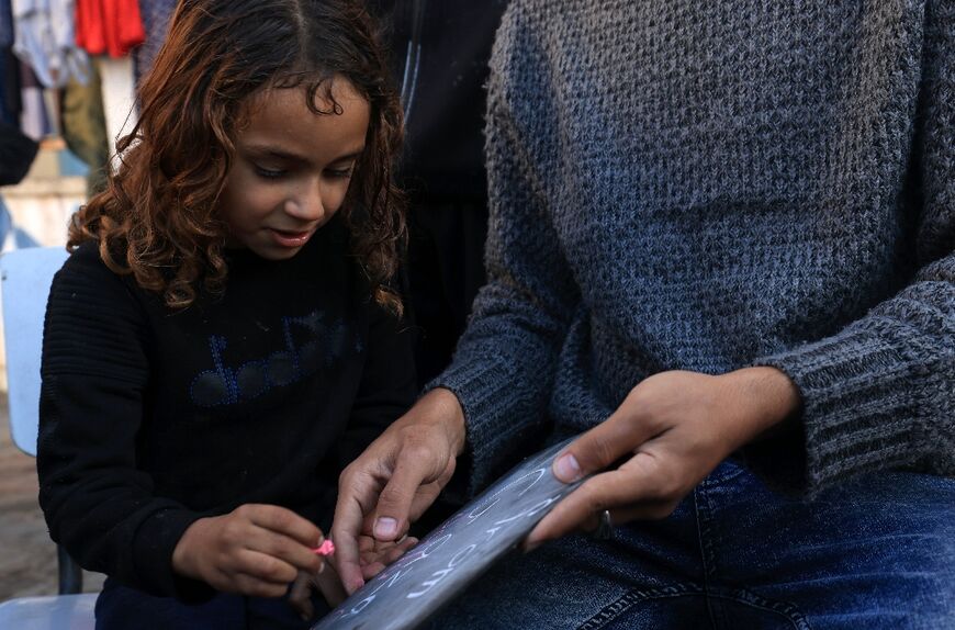 A displaced Palestinian child writes on a board as she follows an English lesson taught by Ennabi