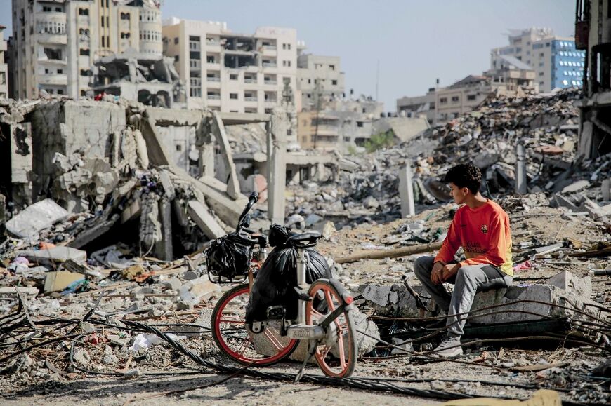 A Palestinian youth sits next to his bicycle amid the rubble of destroyed buildings in Gaza City