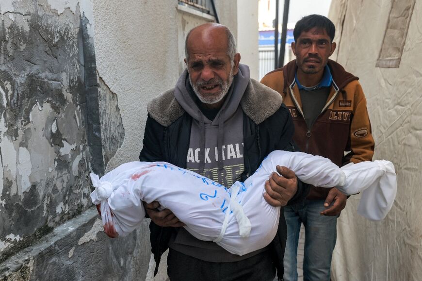 Hani Abu Jamea, a Palestinian from Khan Yunis, follows his father who is carrying the wrapped body of his daughter Sidal who died overnight while sleeping in a tent from a shrapnel fragment