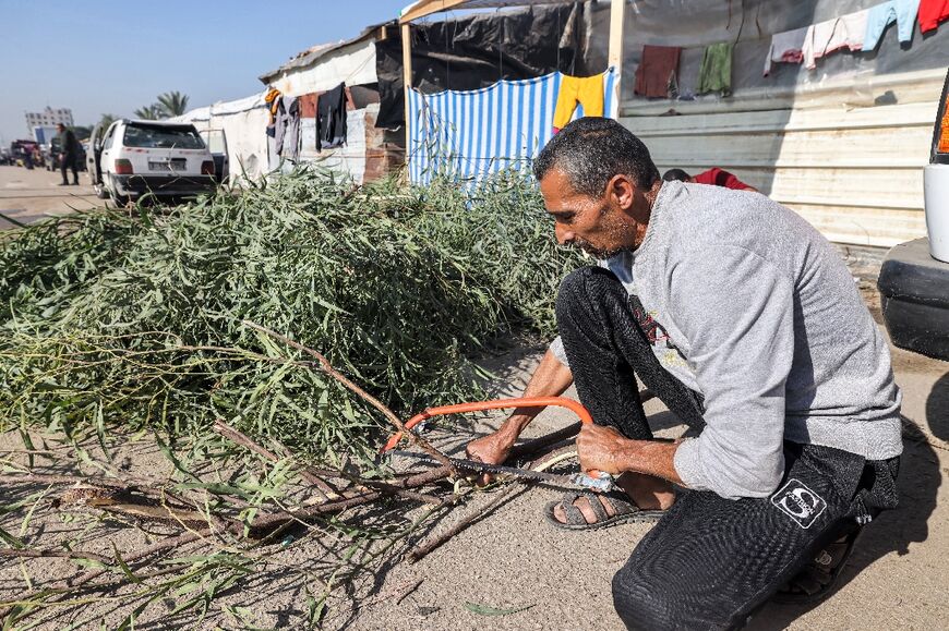 A man cuts tree branches for firewood in Rafah, where fuel and other essential goods are scarce