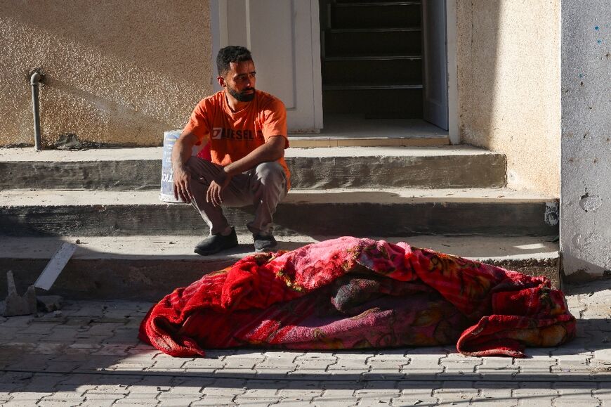 A man sits near the corpse of a person killed in Israeli bombing on Rafah in the southern Gaza Strip