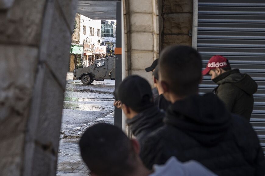 Palestinian youths observe an Israeli army patrol car at the entrance to Jenin refugee camp in the Israeli-occupied West Bank, where violence has surged alongside the Israel-Hamas war