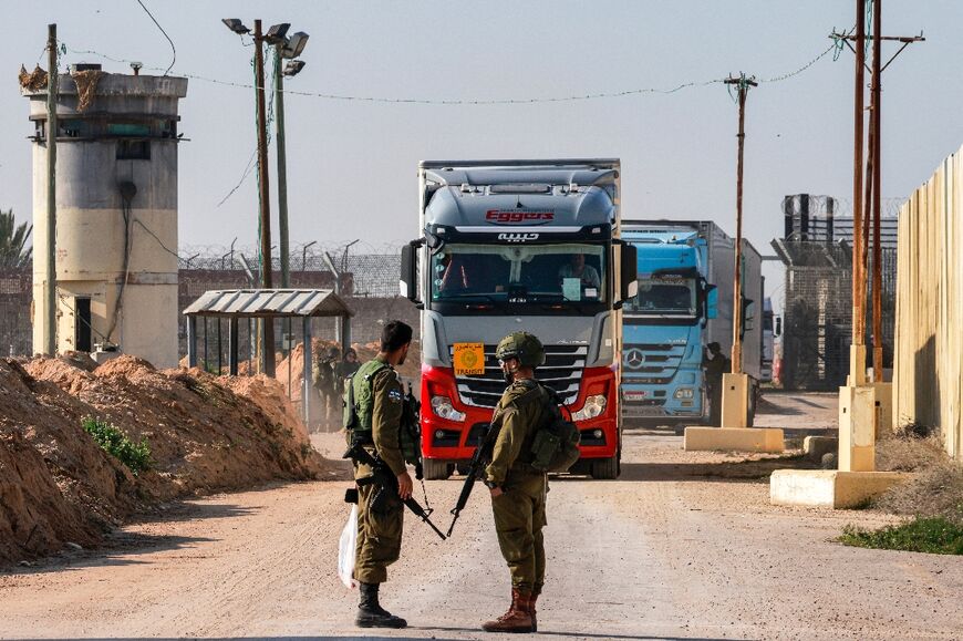 Israeli soldiers stand guard as trucks carrying humanitarian aid move through the Israeli side of the Kerem Shalom border crossing with the southern Gaza Strip
