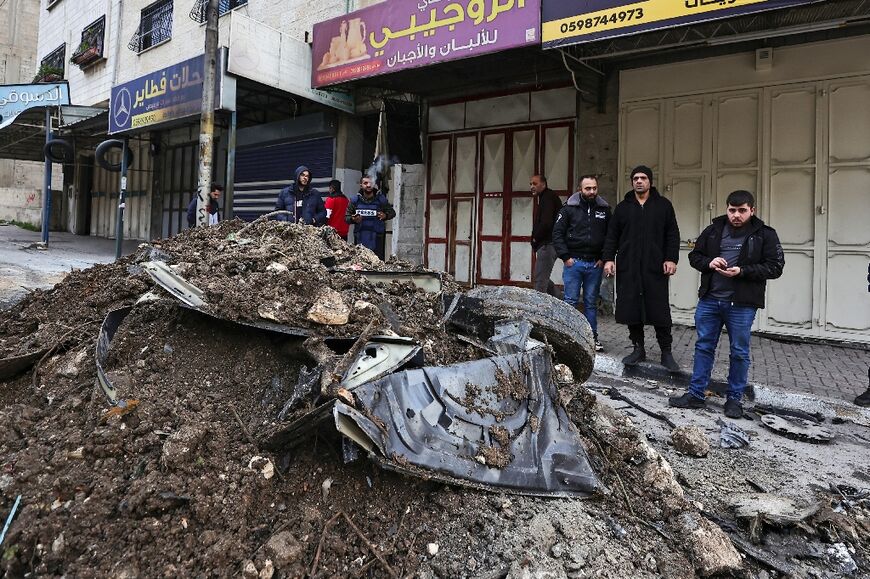 Palestinian onlookers survey the mangled wreckage of a car hit by an Israeli air strike targeting a top militant near the Balata refugee camp in the West Bank city of Nablus