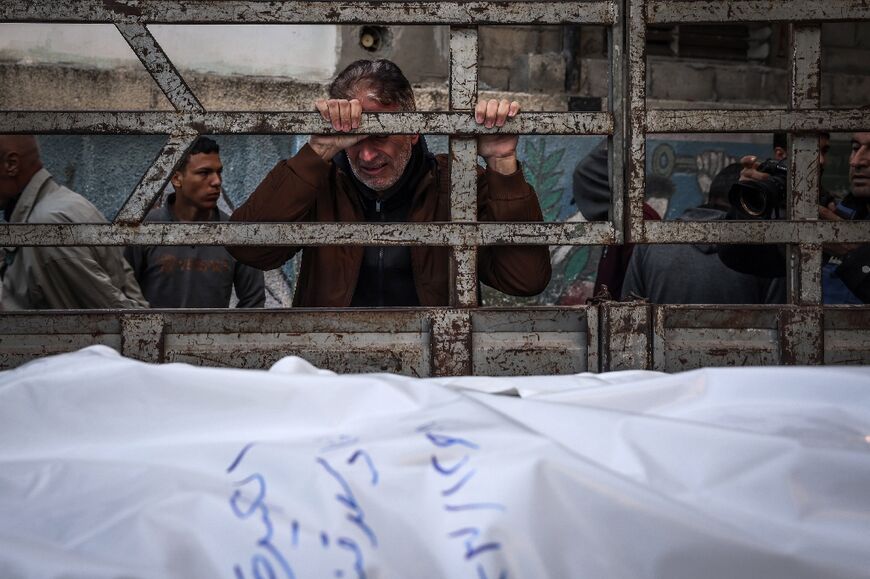 A man mourns at Al-Najjar hospital in Rafah over the shrouded bodies of loved ones killed during Israeli bombardment, on December 29, 2023