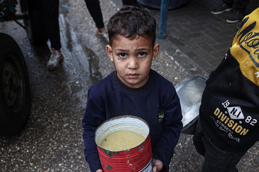 A displaced Palestinian child carries a ration of red lentil soup, distributed by volunteers in Rafah in the southern Gaza Strip on February 18, 2024