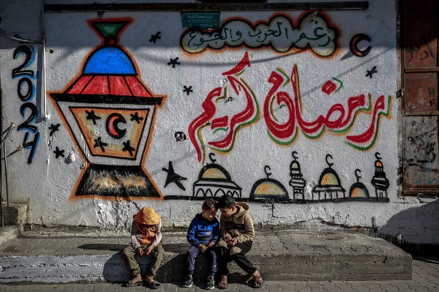 Palestinian children sit in front of Ramadan-themed drawings in Gaza City, in the territory's north where food is particularly scarce