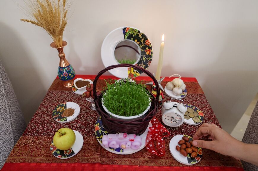 An Iranian decorates a table with "Haft Seen" mostly food and other items that begin with the Persian equivalent of the letter S to mark Nowruz, including an apple, garlic, a coin and green sprouts