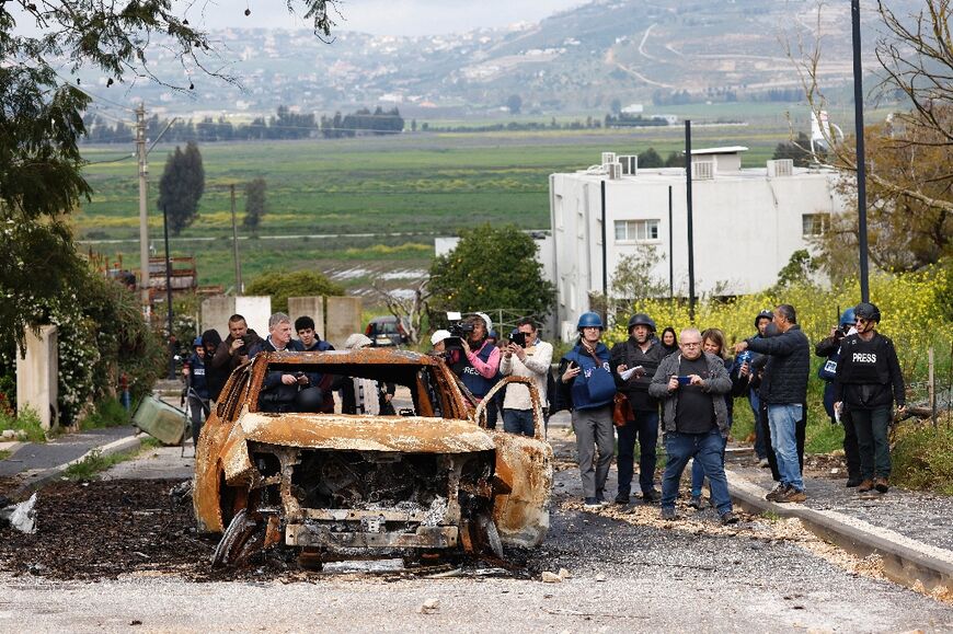 A picture taken during an organised tour shows reporters standing next to a destroyed car in Metula 