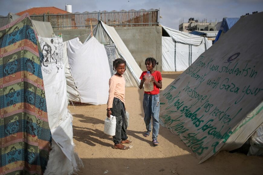 Children carry water containers next to a tent bearing a message of thanks to US students protesting in solidarity with the people of Gaza, at a camp for displaced Palestinians in Rafah, in the southern Gaza Strip 