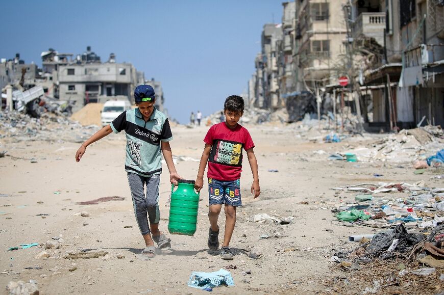 Children carry water as they walk past buildings destroyed during Israeli bombardment in Khan Yunis, southern Gaza