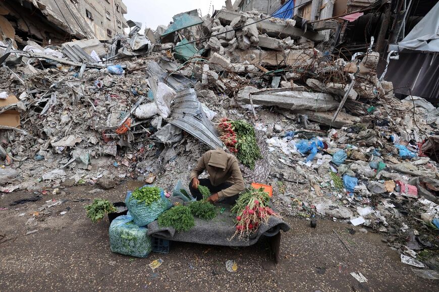 A young Palestinian man sells fresh vegetables in front of a building destroyed in Israeli strikes in Rafah in the southern Gaza Strip on April 7, 2024 
