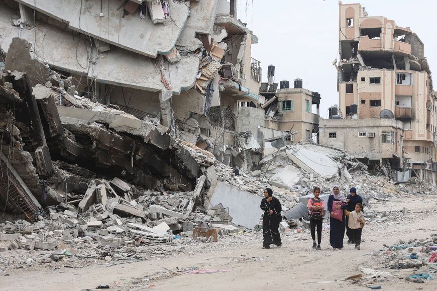 Palestinian women and children walk past the ruins of buildings destroyed by Israeli bombardment in Gaza City