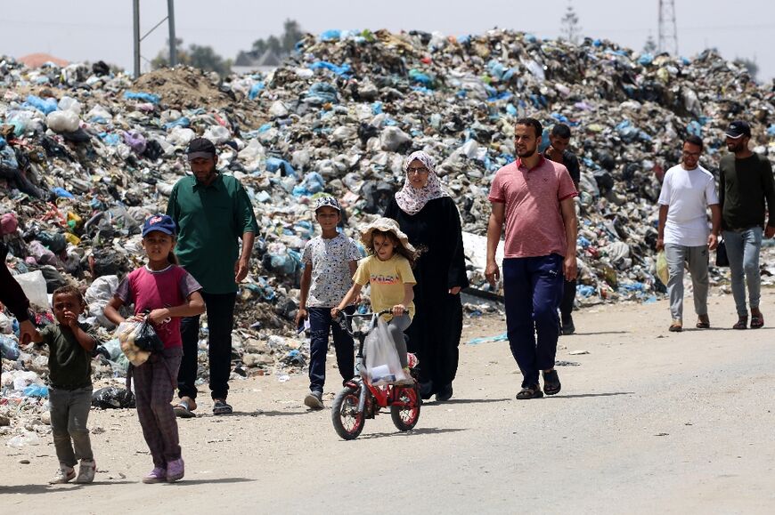 Gazans walk past mounds of garbage piled up near tents set up by displaced people in Khan Yunis