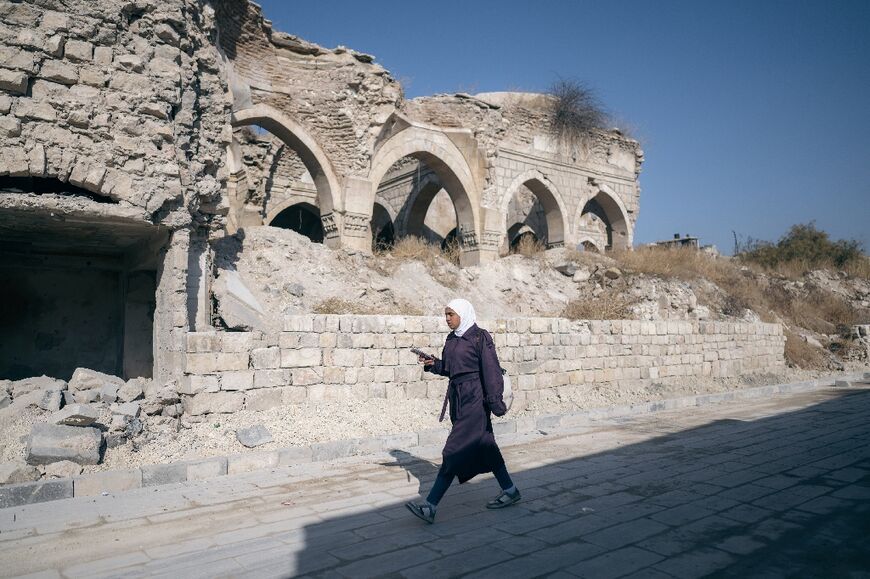 A woman walks past destroyed buildings in Aleppo, whose old city is a UNESCO World Heritage site