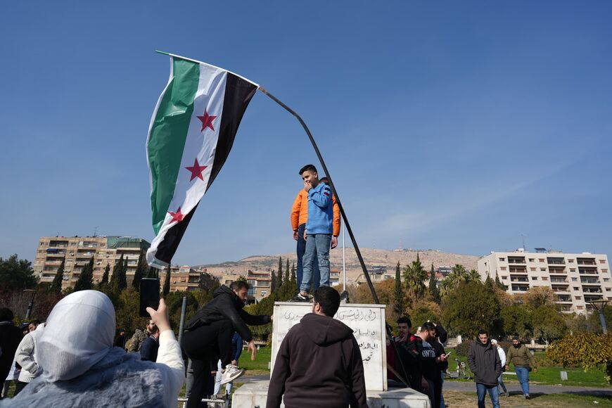 In Damascus, a young boy stands beneath Syria's new flag, which was adopted by activists and rebels during the country's 2011 revolution. Photo taken on December 11, 2024. Photo credit: Morhaf Kiwan.
