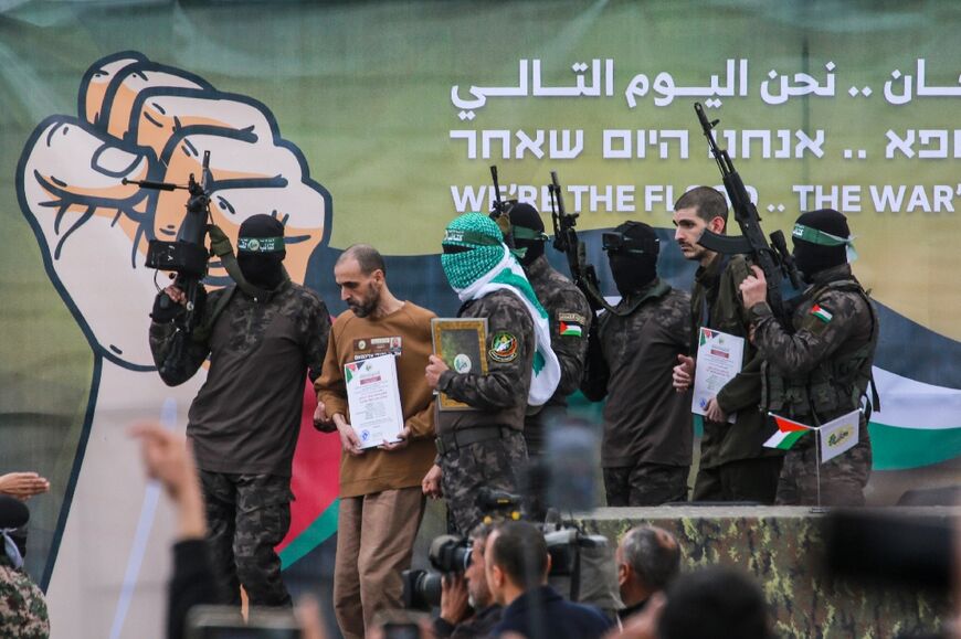 Palestinian Hamas fighters escort Israeli hostages Or Levy (2nd-R) and Eli Sharabi (2nd-L) off a stage before handing them over to a Red Cross team in Deir el-Balah, central Gaza, under the ceasefire's first phase