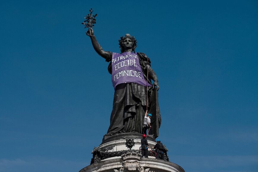 Protesters placing a banner reading 'Patriarchy, ecocide, femicide' on the Statue of the Republic in Paris