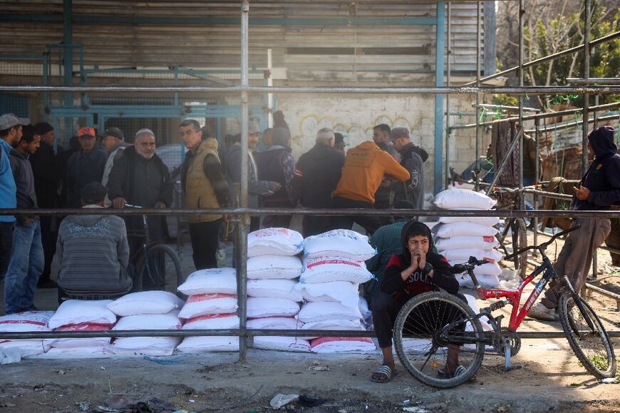 Palestinians queue to receive food aid from an UNRWA distribution center at the Nuseirat refugee camp