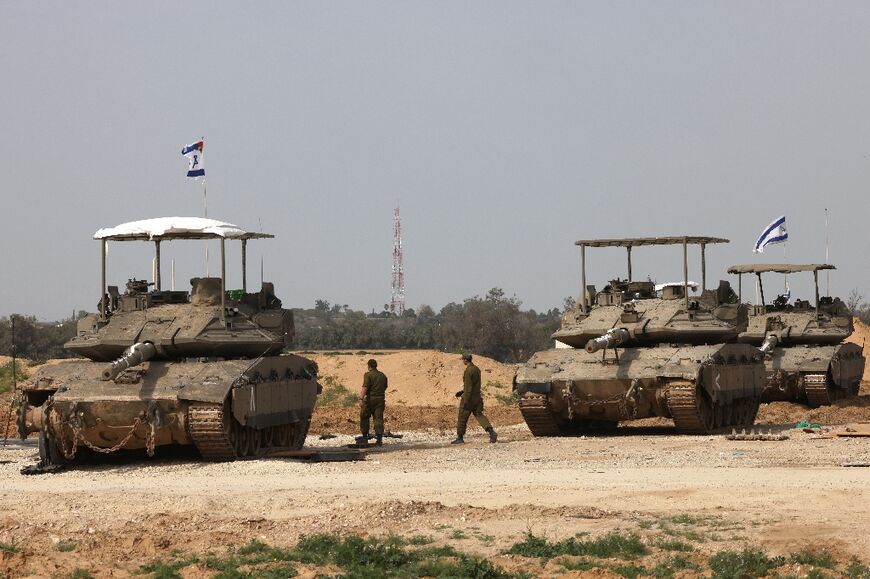 Israeli army soldiers walk past tanks at a position near Israel's southern border with the Gaza Strip