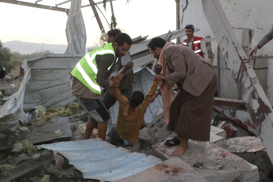Yemeni rescuers pull an injured man from the rubble of the destroyed migrant centre