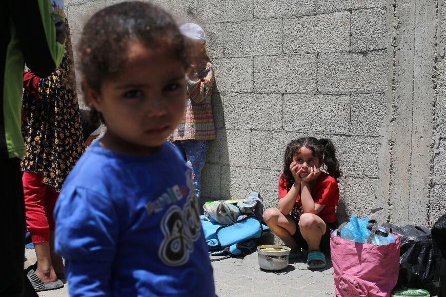 Palestinian children wait near a charity kitchen distributing portions of cooked food at the Nuseirat refugee camp in the central Gaza Strip