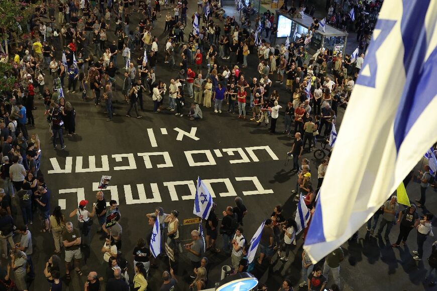 Protesters at a rally in Tel Aviv gather around writing on the asphalt that reads "No innocents in the government" in Hebrew 