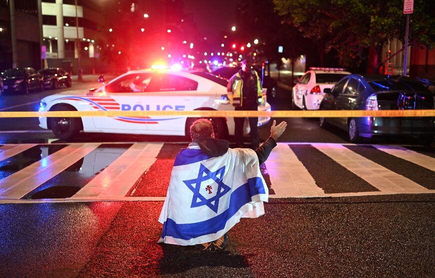 A man draped in the Israeli flag, bearing a cross and the name "Jesus" at its center, gestures as police secure the area outside the Capital Jewish Museum following a shooting that left two people dead in Washington, DC