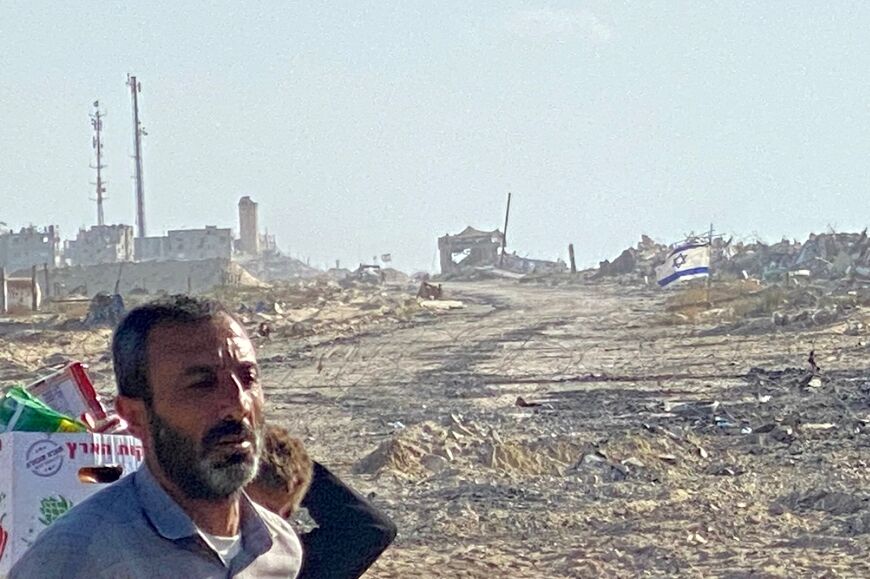 An Israeli flag flies in the distance at a zone where Israeli forces are deployed as displaced Palestinians receive food packages from a US-backed foundation in Rafah