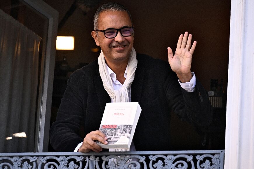 L'écrivain algérien Kamel Daoud, lauréat du Prix Goncourt pour son roman "Houris", salue depuis la fenêtre du restaurant Drouant à Paris, le 4 novembre 2024