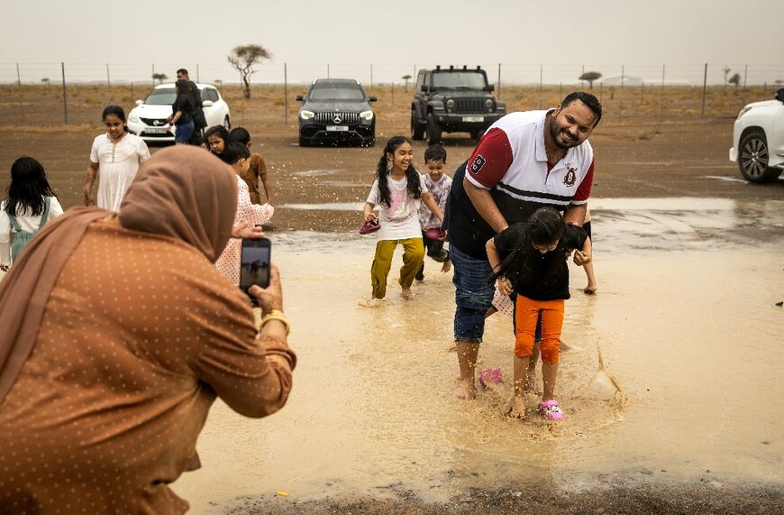 Children and their parents pose for photographs playing in desert puddle.