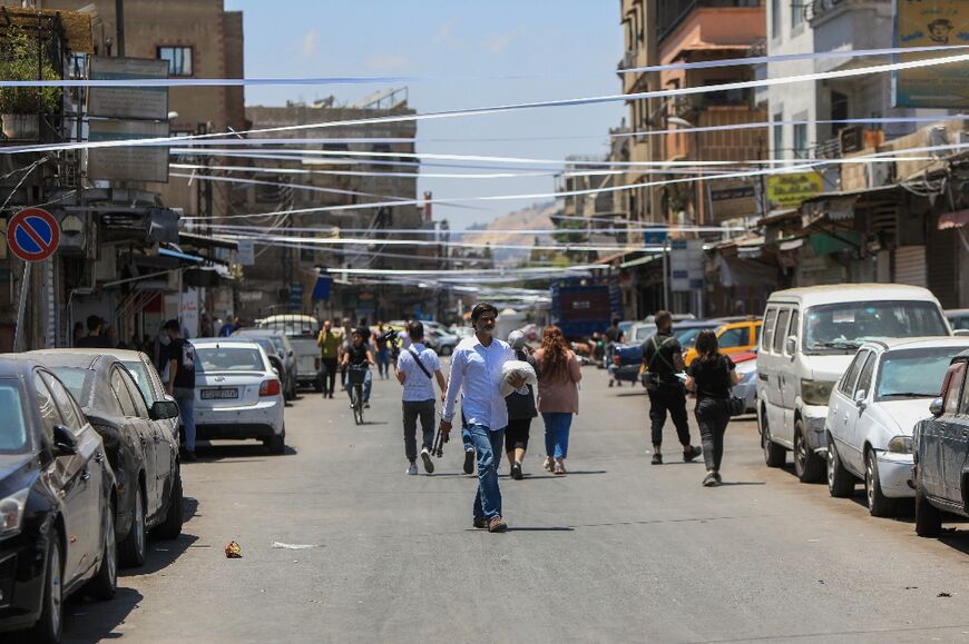 People walk beneath white ribbons stretched across the street in sign of mourning, near the Saint Elias church 
