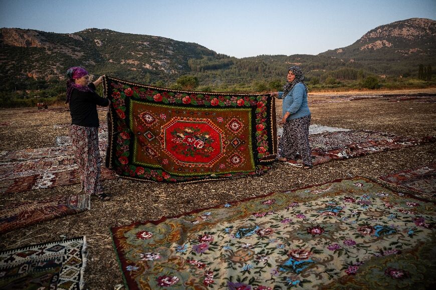 Workers hold a handwoven carpet -- just one of thousands which traders bring to age in the sun to temper overly bright hues and rid them of any unwanted elements