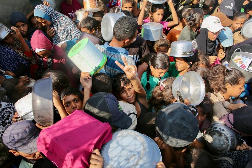 A Palestinian boy flashes the victory sign as he shoves the crowd to receive a hot meal at a charity kitchen in the Mawasi area of Khan Yunis in the southern Gaza Strip on July 22, 2025