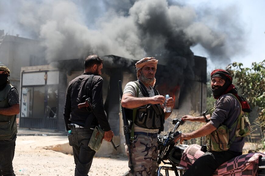 Bedouin fighters watch on impassively as a building goes up in smoke in the village of Al-Mazraa outside Sweida.