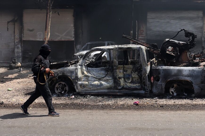 An armed Bedouin walks past a burnt out vehicle in the Syrian village of Al-Mazraa, outside Sweida as clashes flare with Druze fighters.